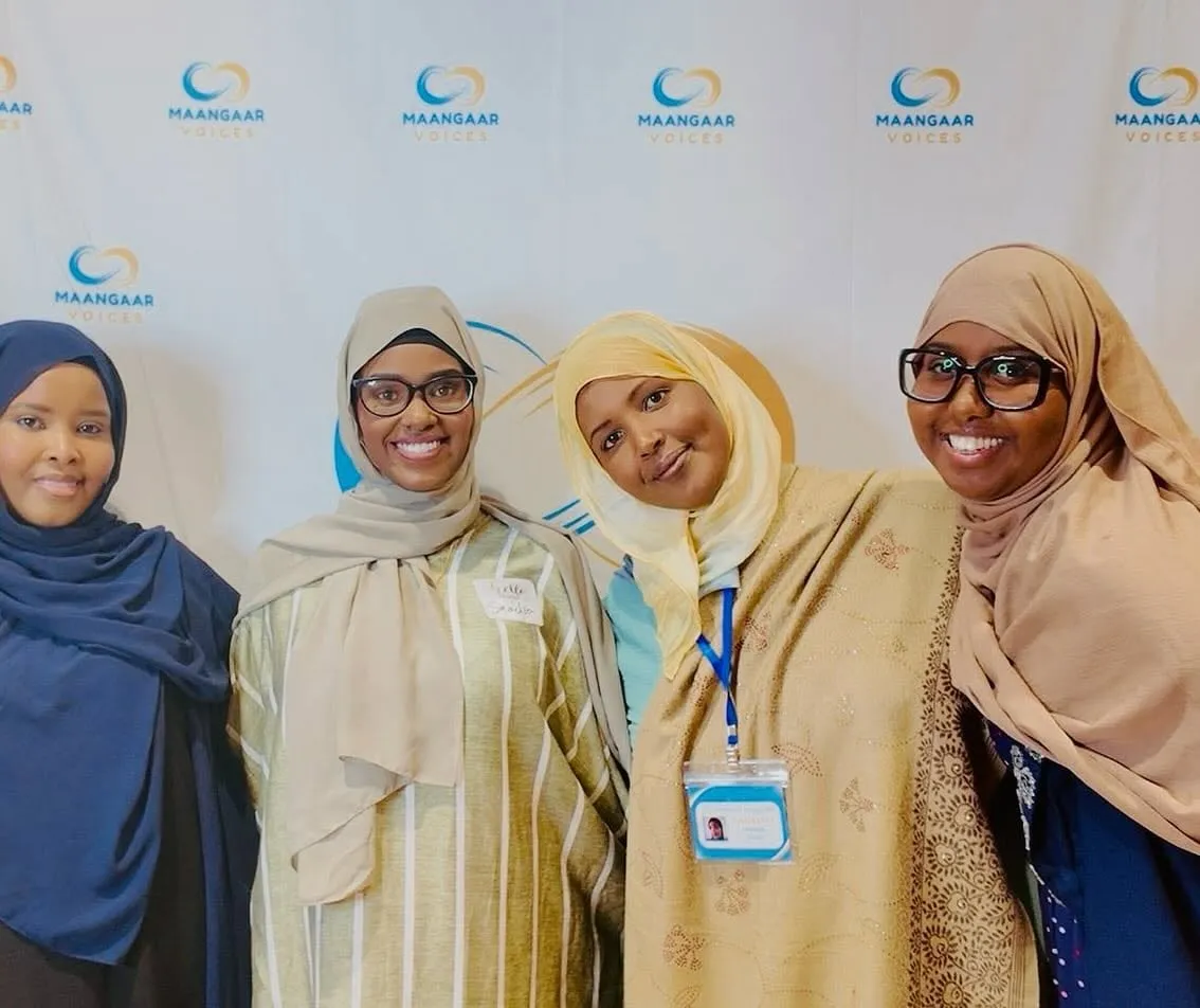 Four women smile together in front of the Maangaar Voices backdrop at Maangaar Summit 2025.