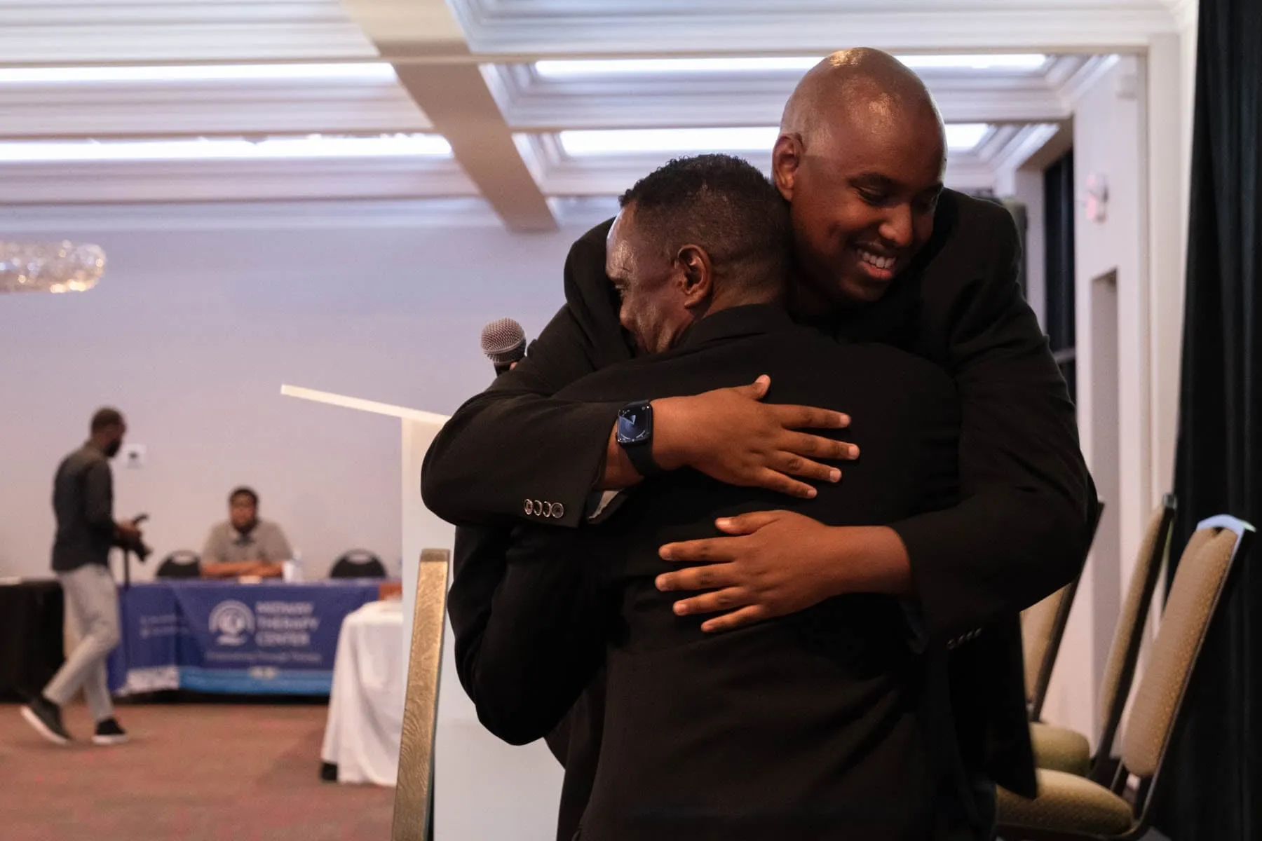 Abdikareem Hurreh, host of the Maangaar Summit, hugs Mahad Dahir, a 23-year-old autistic self-advocate, as he walks off the stage.
