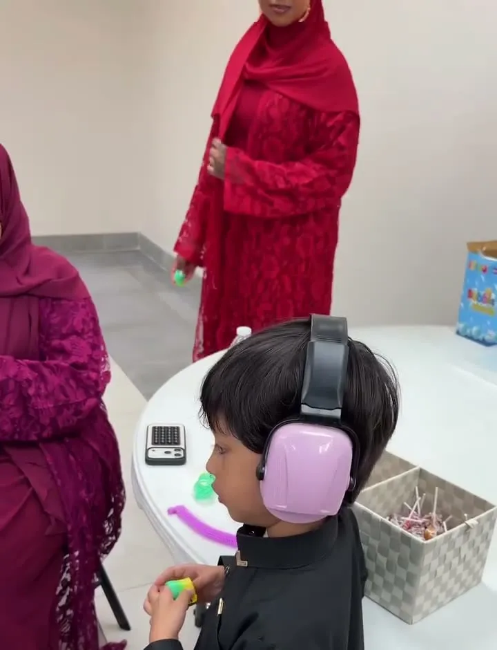 A boy wearing pink ear defenders works at an activity table during the Eid al-Adha prayer.