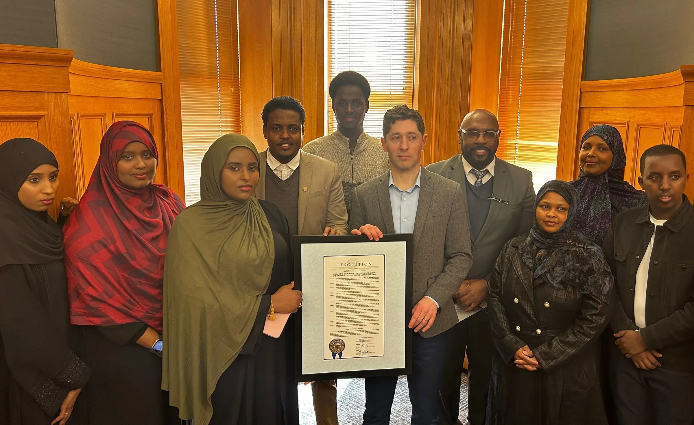 Maangaar Voices members and community advocates hold the framed resolution with the Mayor’s Office.