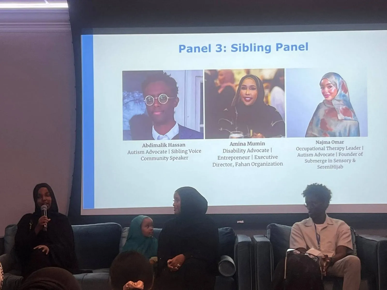 The Sibling Panel on stage beneath a slide reading Panel 3: Sibling Panel, introducing Abdimalik Hassan, Amina Mumin and Najma Omar.
