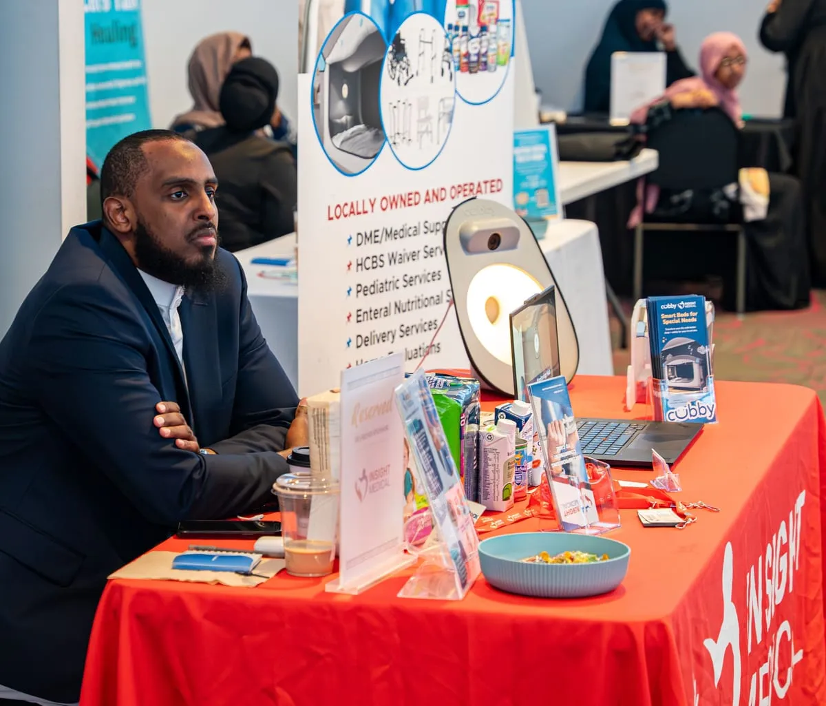 A vendor welcomes attendees at an exhibitor table.