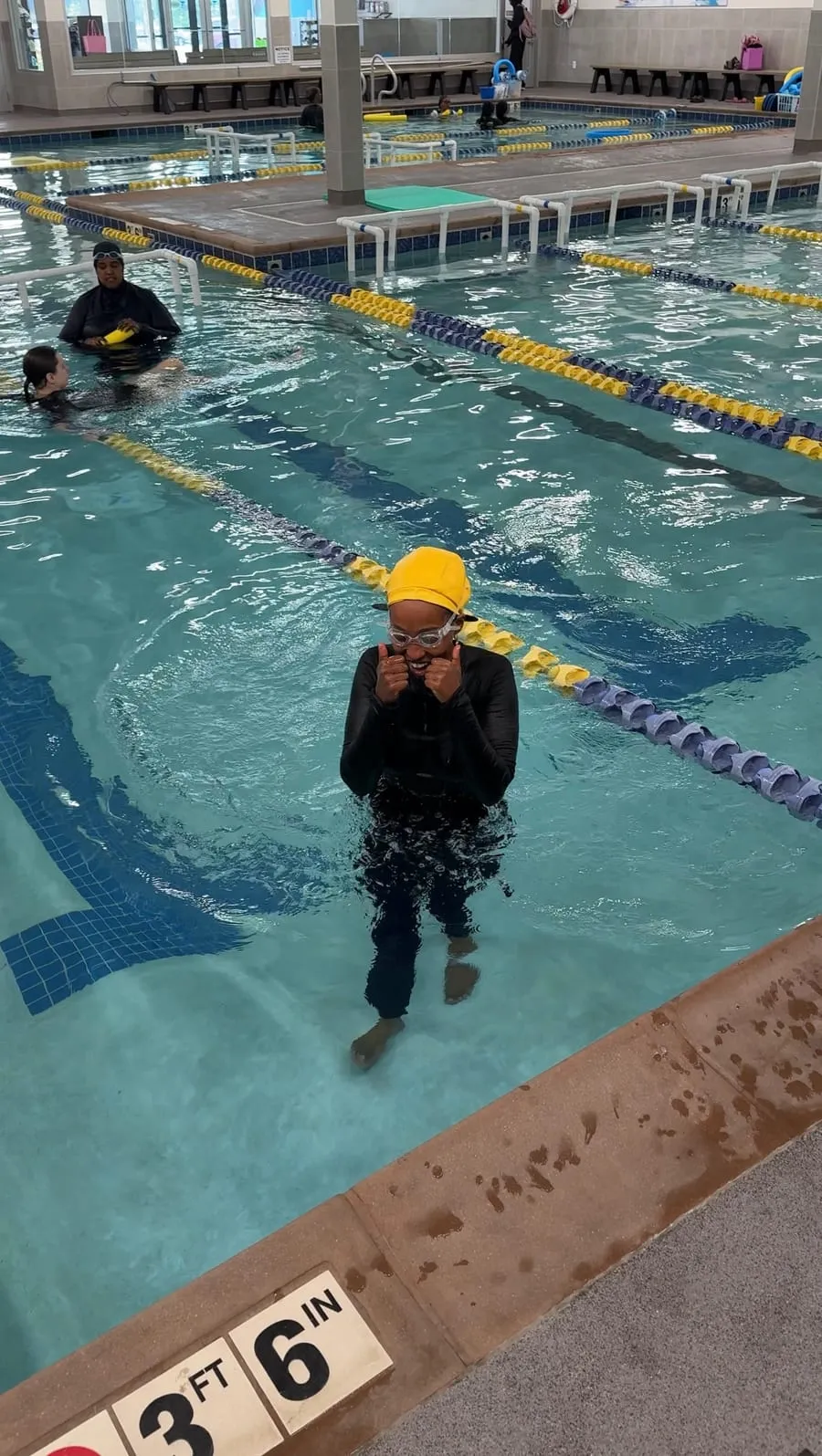 A swimmer in a yellow cap and goggles stands in the pool during a lesson.
