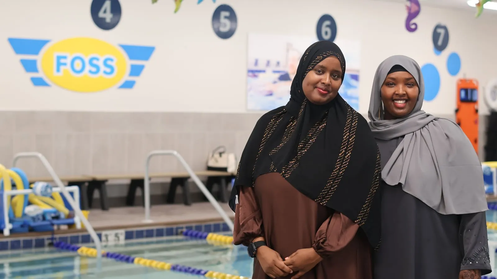 Board chair Anisa Hagi-Mohamed and board member Amina Adan smile beside the pool at FOSS Swim School in Burnsville.